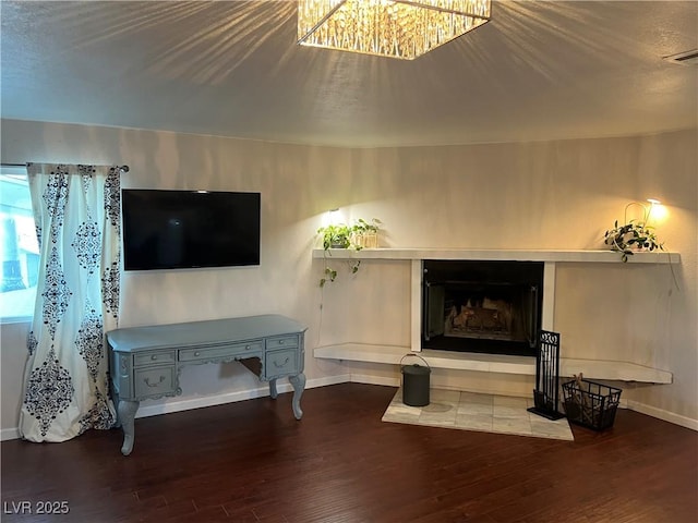 living room featuring visible vents, baseboards, a fireplace with raised hearth, and wood finished floors