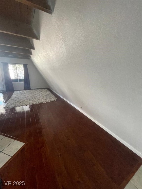 additional living space with baseboards, a textured ceiling, wood finished floors, and vaulted ceiling with beams