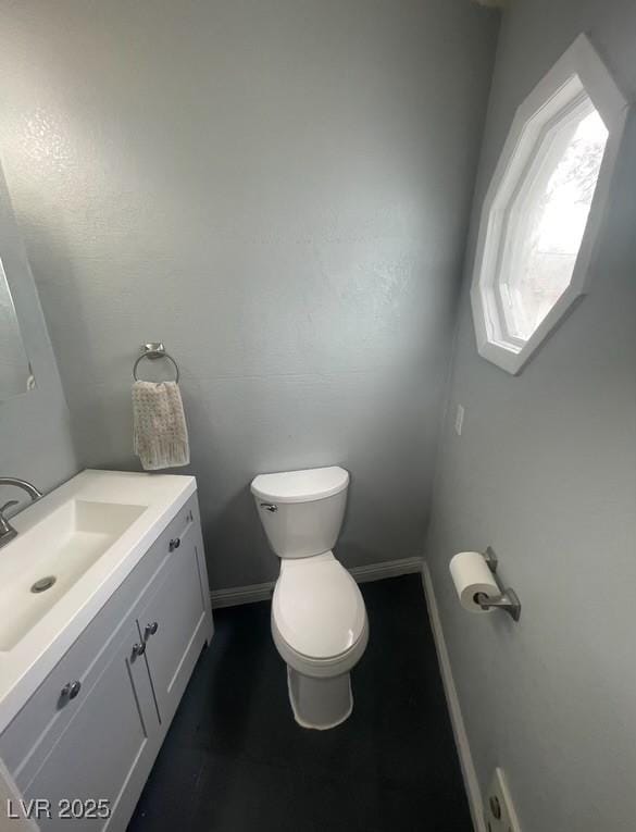 half bathroom with baseboards, toilet, and vanity