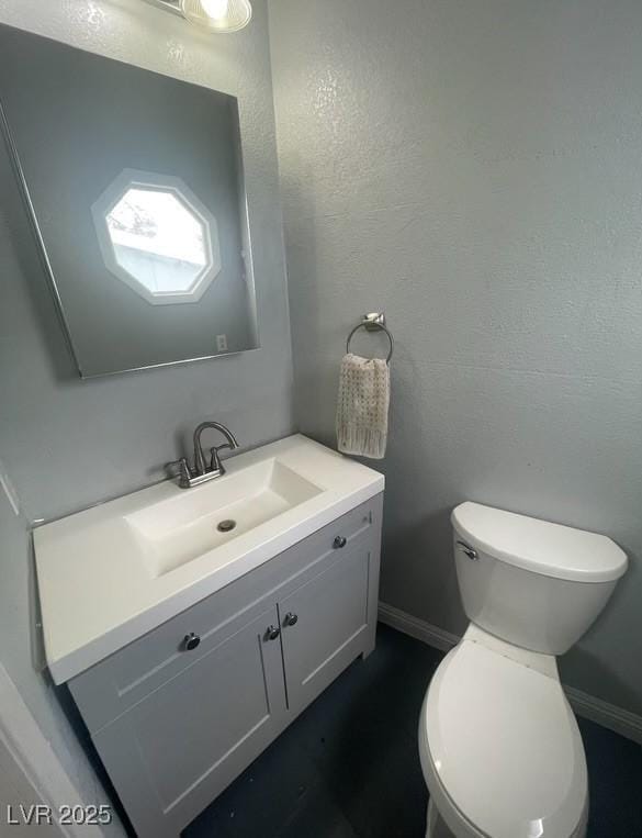 bathroom featuring vanity, toilet, a textured wall, and baseboards