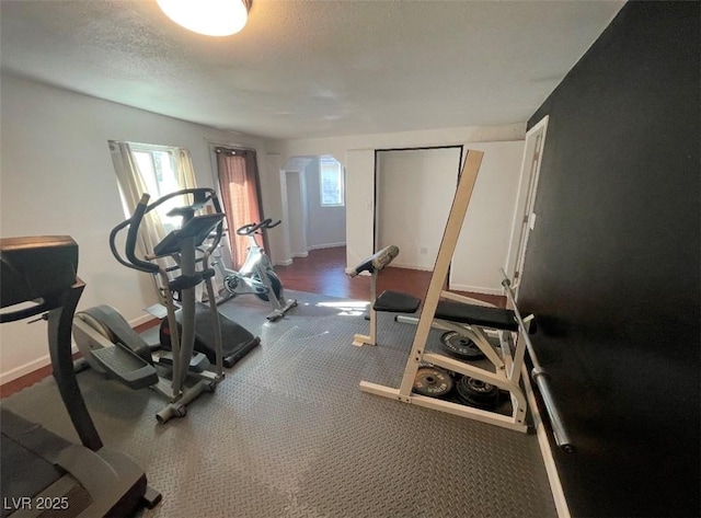 workout area featuring baseboards, arched walkways, and a textured ceiling