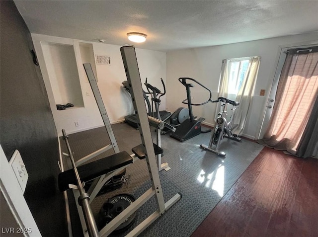 workout room with visible vents, baseboards, a textured ceiling, and wood finished floors