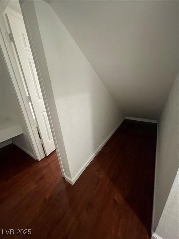 hallway featuring lofted ceiling, baseboards, and dark wood-style flooring