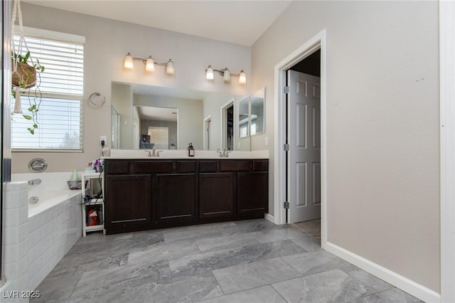 full bathroom with double vanity, a bath, baseboards, and a sink