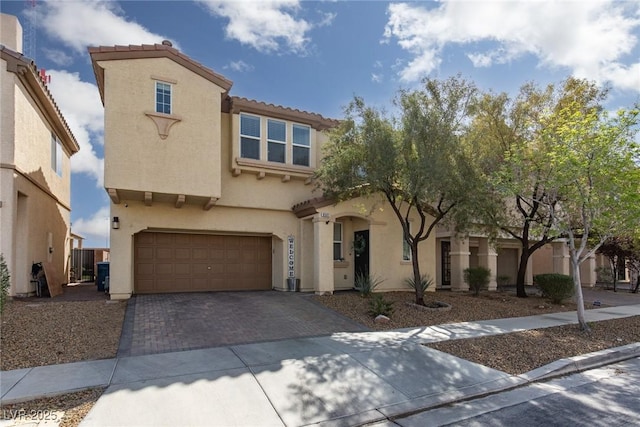 mediterranean / spanish home featuring decorative driveway, a tile roof, an attached garage, and stucco siding