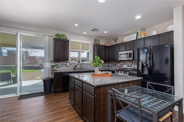 kitchen with visible vents, black appliances, a sink, backsplash, and dark wood-style flooring