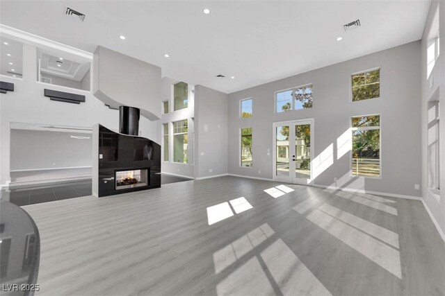 living area with a high ceiling, french doors, visible vents, and a multi sided fireplace