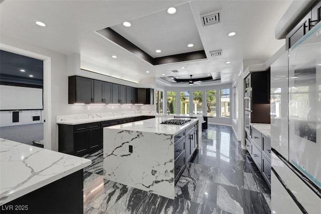 kitchen featuring stainless steel gas cooktop, light stone counters, recessed lighting, a large island, and a raised ceiling