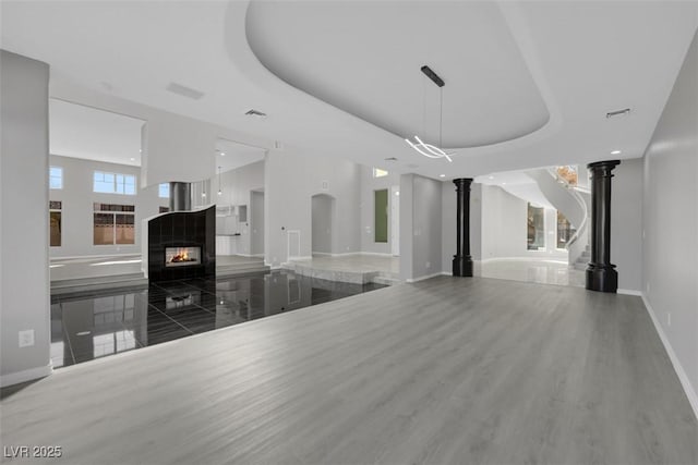 unfurnished living room featuring a multi sided fireplace, a raised ceiling, baseboards, and ornate columns