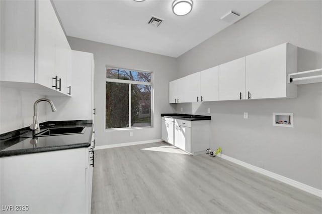 kitchen with a sink, visible vents, baseboards, and white cabinets