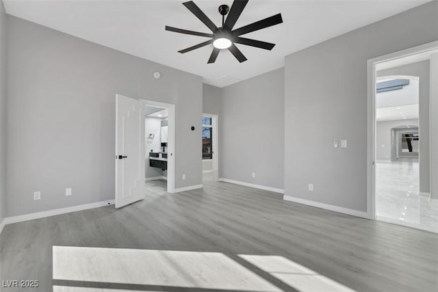 empty room featuring baseboards, arched walkways, wood finished floors, and a ceiling fan