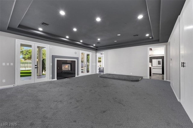 unfurnished living room featuring a glass covered fireplace, a raised ceiling, french doors, and visible vents