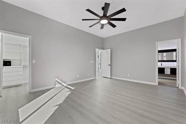 unfurnished bedroom with a spacious closet, wood finished floors, baseboards, and ceiling fan