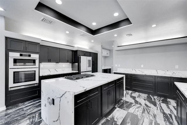 kitchen featuring visible vents, refrigerator, gas stovetop, a raised ceiling, and a center island