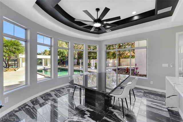 sunroom with a raised ceiling, a healthy amount of sunlight, and a ceiling fan