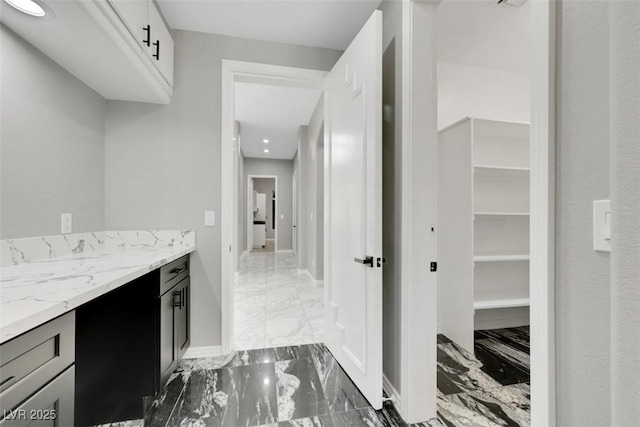 interior space with light stone counters, marble finish floor, dark cabinetry, and baseboards