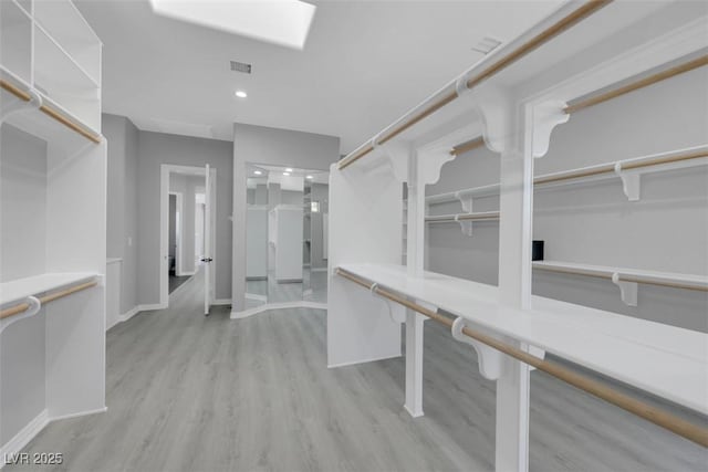 spacious closet with visible vents, a skylight, and wood finished floors