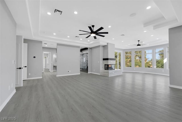 unfurnished living room featuring visible vents, a multi sided fireplace, a tray ceiling, recessed lighting, and wood finished floors