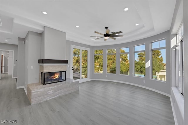 unfurnished living room with baseboards, a premium fireplace, recessed lighting, wood finished floors, and a raised ceiling