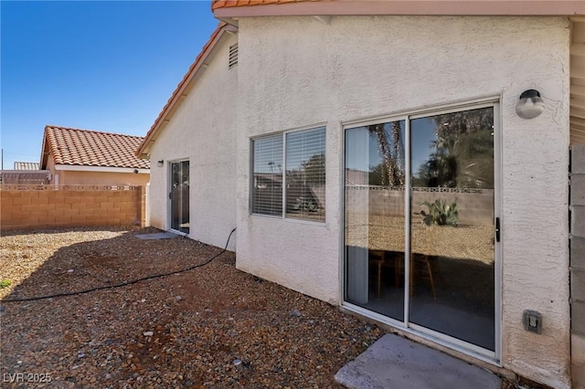 rear view of property featuring a tiled roof, fence, and stucco siding