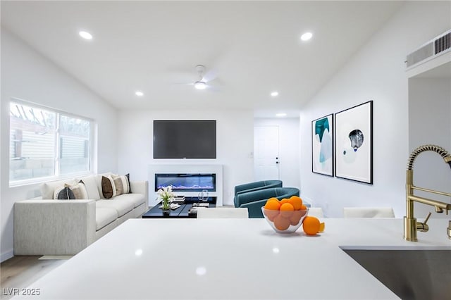 living room with visible vents, a ceiling fan, wood finished floors, a glass covered fireplace, and recessed lighting