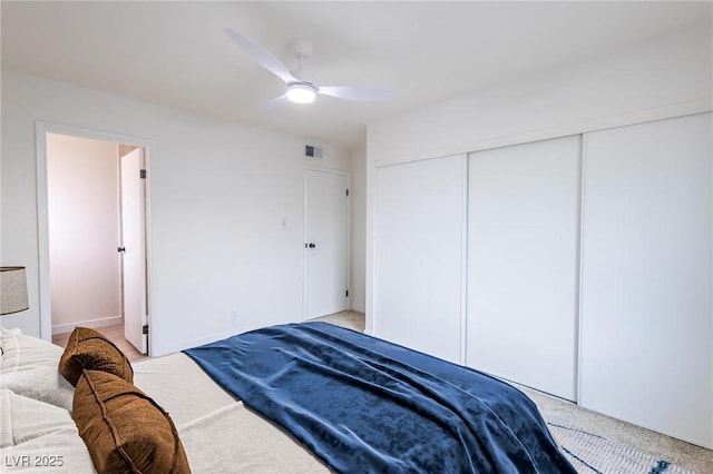 bedroom with a closet, light colored carpet, visible vents, and ceiling fan