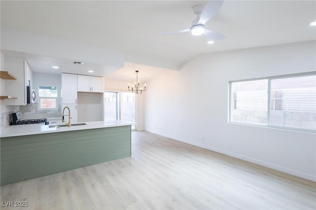 kitchen featuring stainless steel microwave, open shelves, a peninsula, stove, and a sink