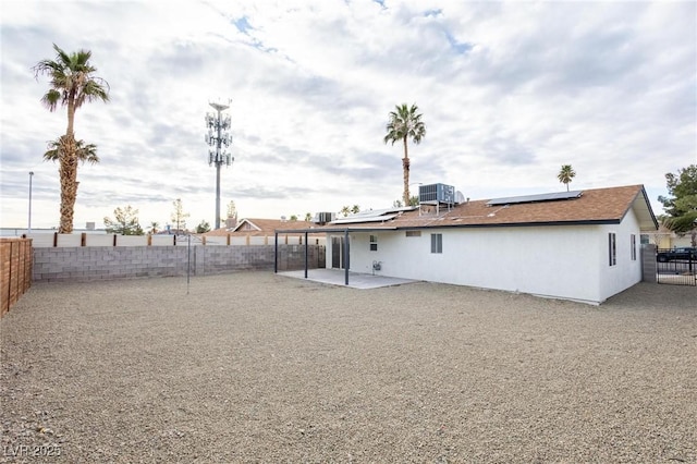 rear view of house with roof mounted solar panels, central AC, a fenced backyard, and a patio area