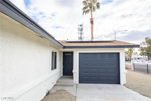 view of exterior entry featuring stucco siding, roof mounted solar panels, fence, concrete driveway, and a garage