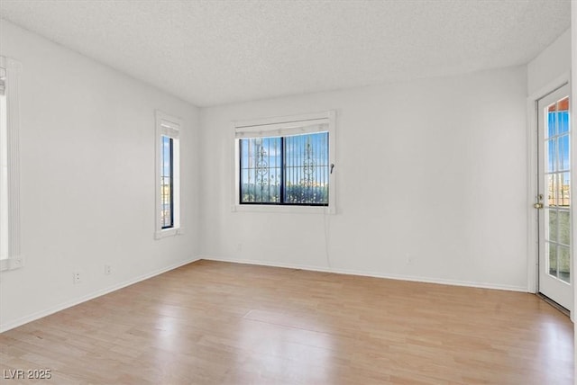 empty room featuring baseboards, light wood-type flooring, and a textured ceiling