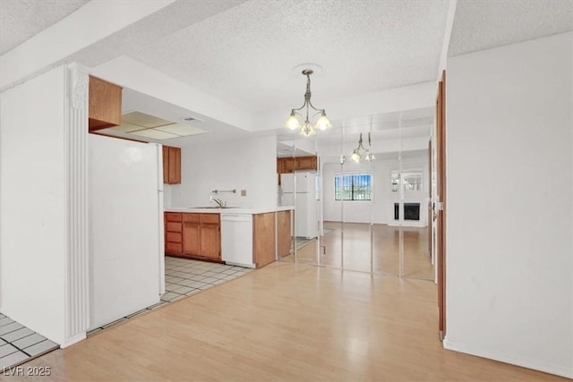 kitchen featuring white appliances, brown cabinetry, light wood finished floors, an inviting chandelier, and light countertops