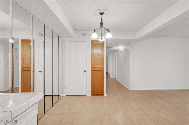 unfurnished dining area with visible vents, a textured ceiling, an inviting chandelier, light wood finished floors, and baseboards