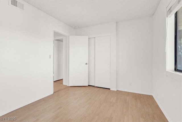 unfurnished bedroom with visible vents, multiple windows, baseboards, and wood finished floors