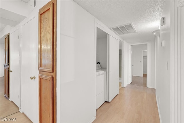 hallway featuring visible vents, light wood-style floors, and a textured ceiling