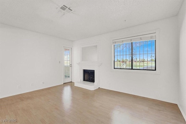 unfurnished living room with visible vents, a fireplace with raised hearth, a textured ceiling, wood finished floors, and baseboards