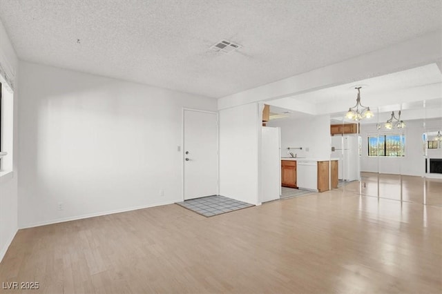 unfurnished living room with visible vents, a textured ceiling, an inviting chandelier, and light wood finished floors