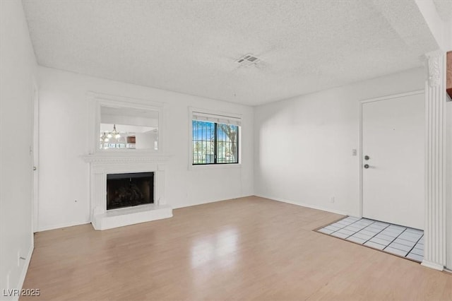 unfurnished living room with visible vents, a fireplace with raised hearth, a textured ceiling, and wood finished floors