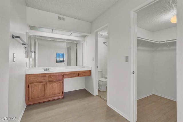 bathroom featuring visible vents, toilet, vanity, wood finished floors, and a textured ceiling