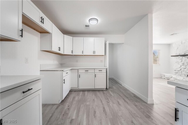 kitchen with visible vents, light wood-style flooring, white cabinetry, light countertops, and baseboards