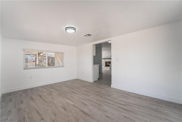 spare room with a lit fireplace, visible vents, baseboards, and light wood-style floors