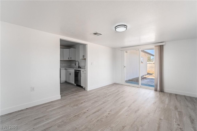 unfurnished living room with visible vents, light wood-type flooring, baseboards, and a sink