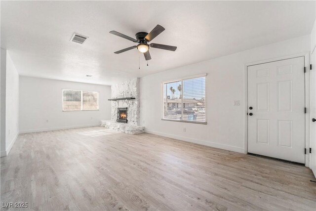 unfurnished living room with visible vents, baseboards, ceiling fan, a stone fireplace, and light wood-style flooring