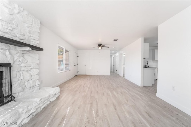 unfurnished living room featuring a stone fireplace, a ceiling fan, light wood-type flooring, and baseboards