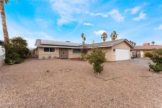 ranch-style home with a gate, roof mounted solar panels, fence, concrete driveway, and an attached garage