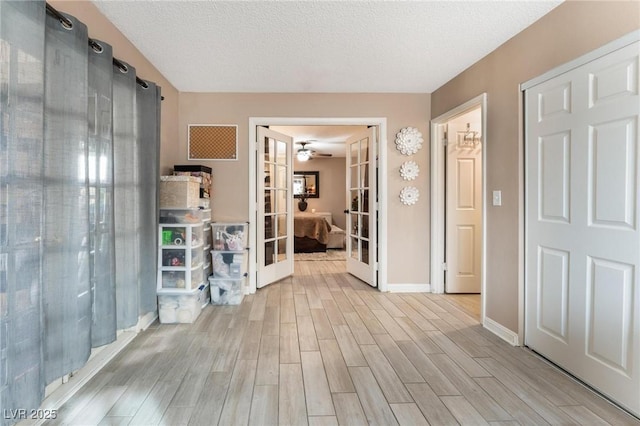 corridor with french doors, a textured ceiling, baseboards, and wood tiled floor