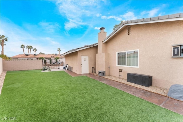 back of property with a fenced backyard, stucco siding, a chimney, and a yard