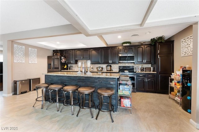 kitchen featuring light stone countertops, a center island with sink, stainless steel appliances, a kitchen breakfast bar, and tasteful backsplash