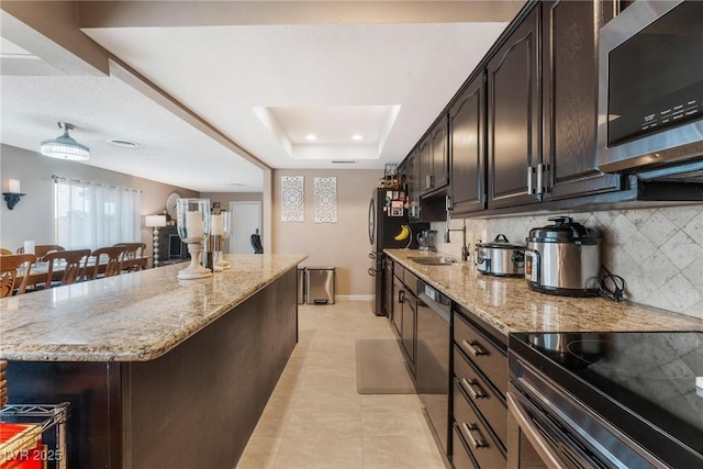 kitchen with light stone counters, a tray ceiling, a kitchen island, and appliances with stainless steel finishes