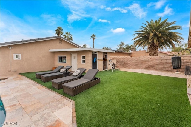 rear view of house with a patio, a lawn, fence, and stucco siding