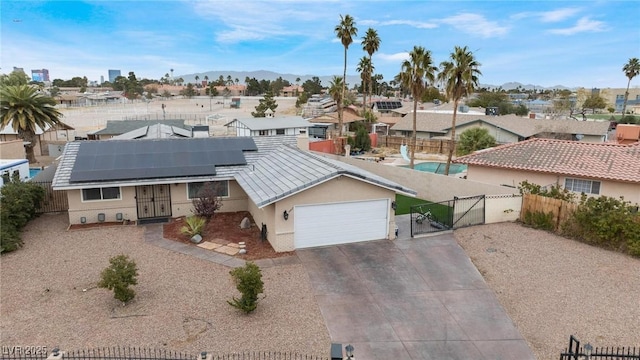 view of front of home with driveway, a gate, roof mounted solar panels, fence, and a garage